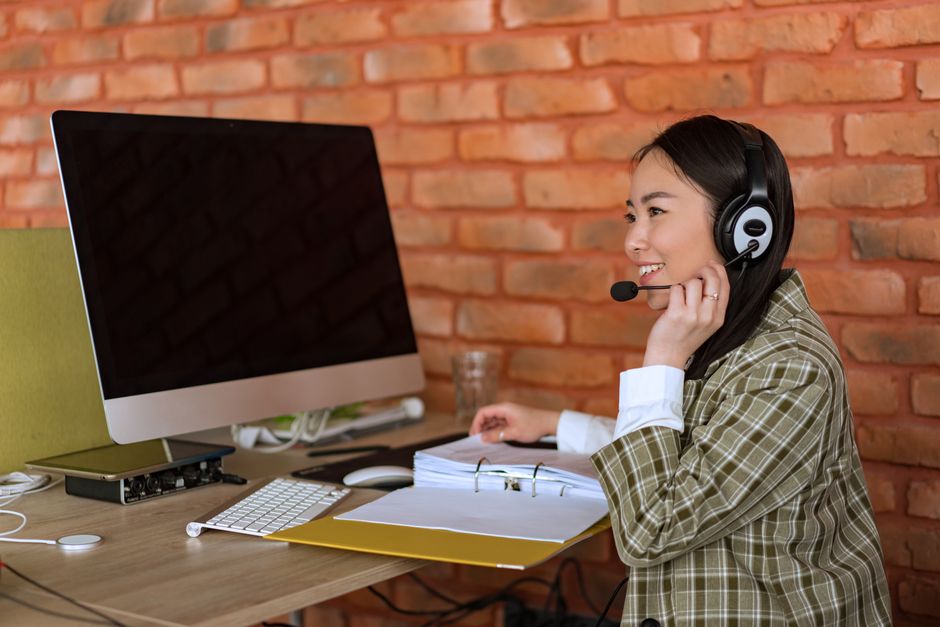 Agente de call center feminina sorridente trabalhando na mesa com computador e headset.