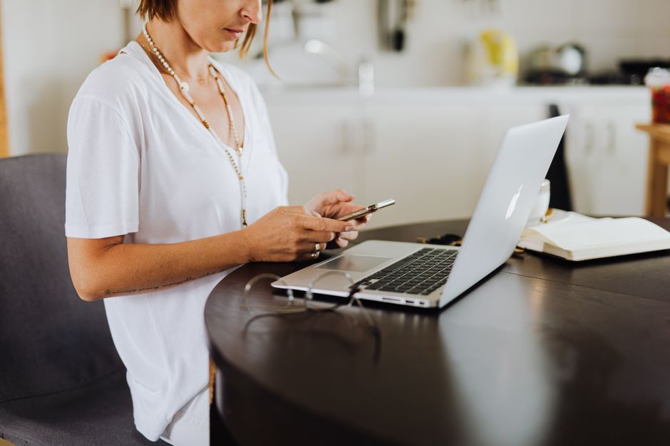Uma mulher multitarefa com seu smartphone e laptop em um ambiente de home office.