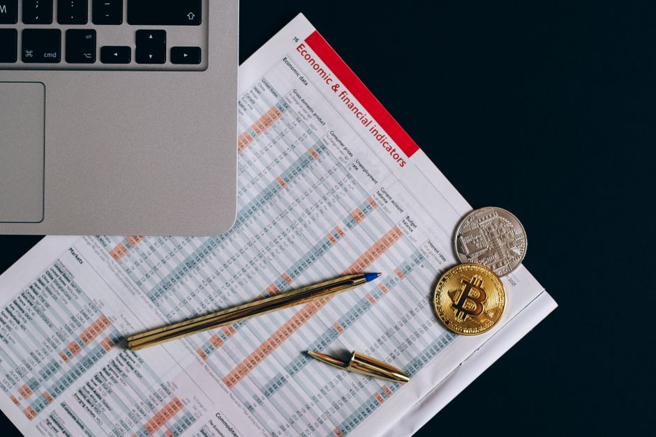 Vista superior de moedas de bitcoin em documentos financeiros ao lado de um teclado de laptop.