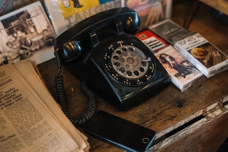 Uma cena nostálgica de um clássico telefone rotativo cercado por fitas e jornais sobre uma superfície de madeira.