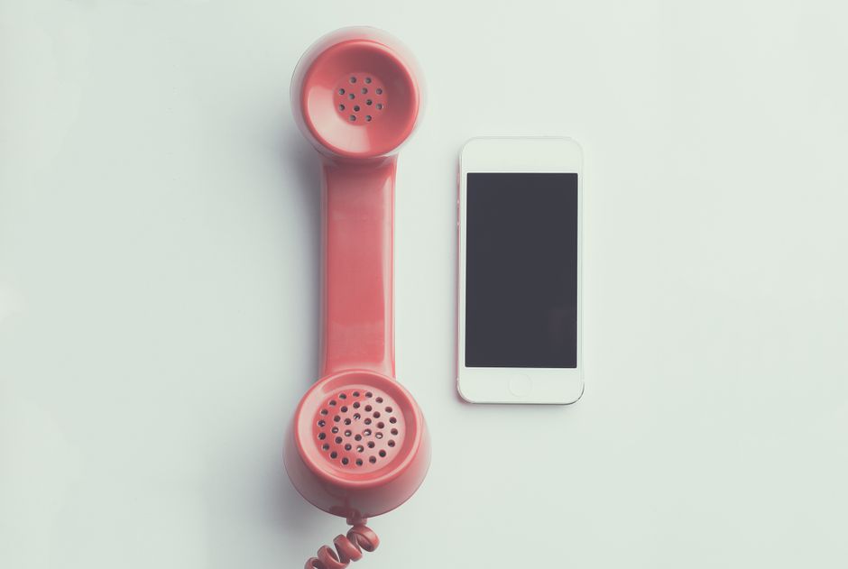 Comparação de um receptor de telefone vintage rosa e um smartphone moderno sobre um fundo simples.
