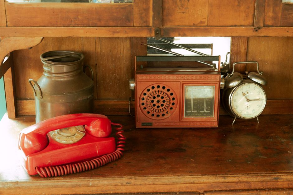 Uma cena vintage com um telefone vermelho de disco, um rádio antigo e um relógio antigo em uma prateleira de madeira.