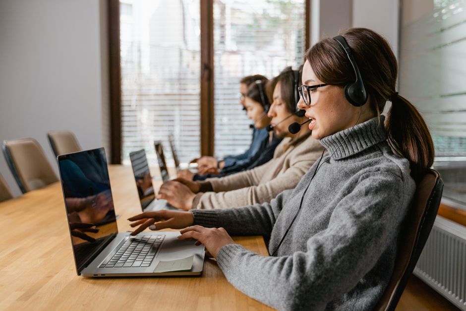 Equipe profissional de atendimento ao cliente trabalhando em um ambiente de escritório moderno com fones de ouvido e laptops.